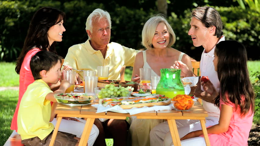 Extended Family Group Sitting Down To Meal As Grandmother Serves Food ...