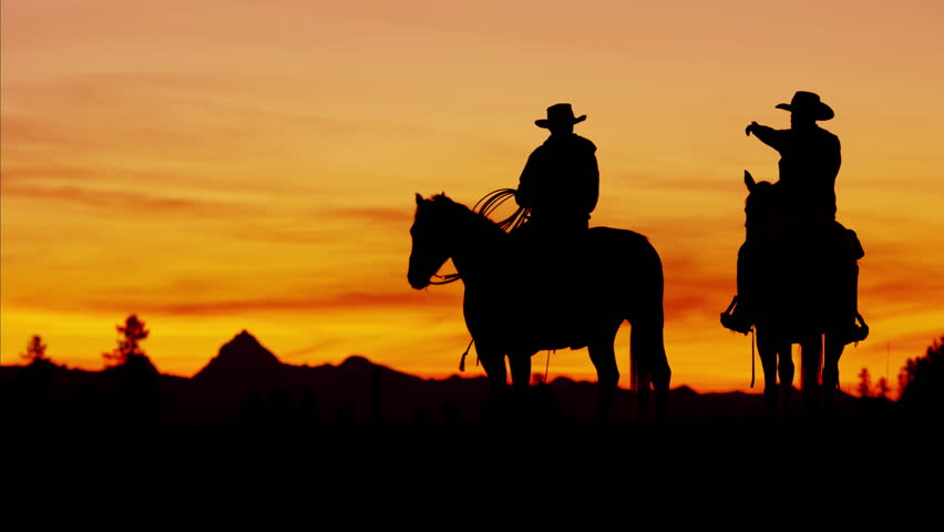 Dusk Shot Of Four Cowboys Riding Off Into The Sunset Towards Mountains ...