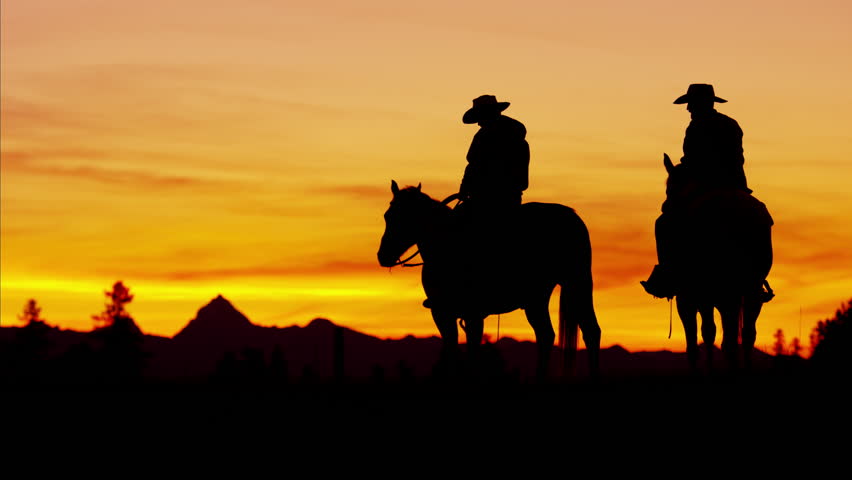 Dusk Shot Of Four Cowboys Riding Off Into The Sunset Towards Mountains ...